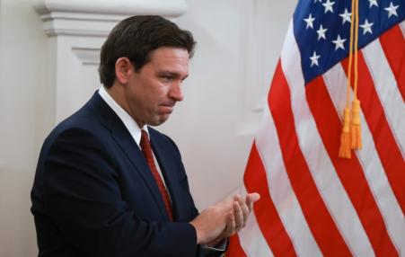 Photo of DeSantis in looking at his cell phone in front of a flag.
