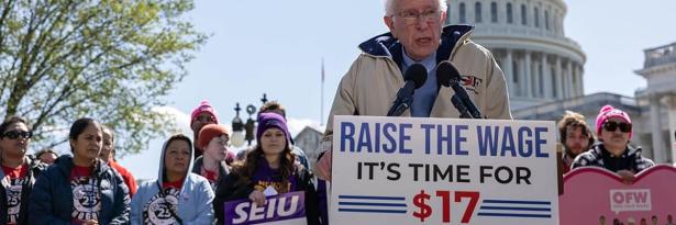 Bernie Sanders at a podium in from of the US Capitol people rallying with signs saying Raise the minimum wage.  Time for $17 and hour.