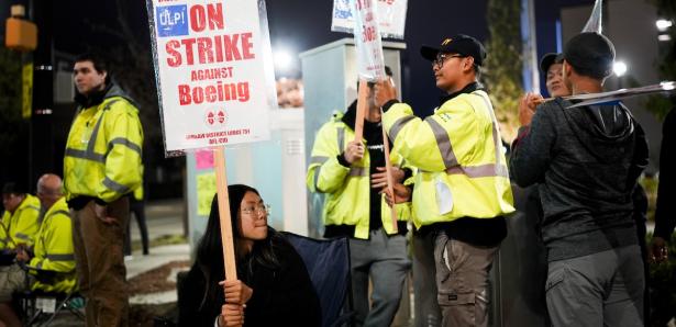 Workers in yellow jackets holding Strike Against Boeing signs.