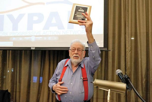 Eddie Kay speaking with his arm raised and  a book in his hand.