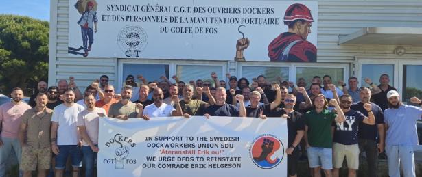 Photo of a group of French dockworkers with raised fists and a banner in support of a Swedish dockworker  