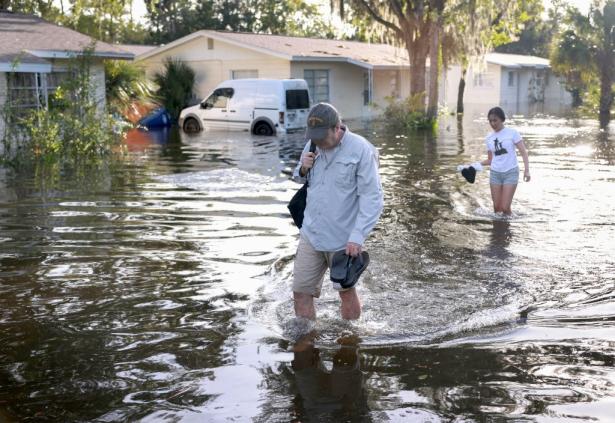 Two people walking through flooded streets with houses in the background.