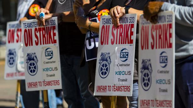 Photo of strike signs on sticks with workers hands leaning on them.   