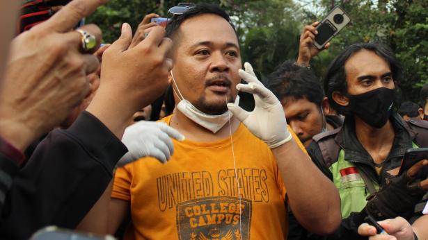 Man with a needle through his lower lip in the foreground amongst a crowd. lips