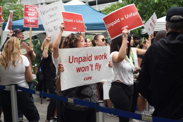 Photo of people rallying with signs that say "Unpaid work won't fly"d