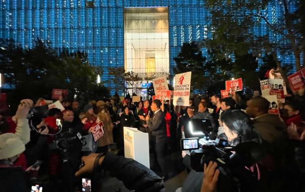 Photo of a rally with signs in front of Conde Nast office building focused on a speaker at the podium.   