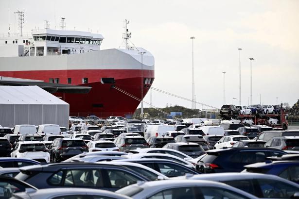 A photo of a parking lot of tesla cars in the foreground and a ship in background. 