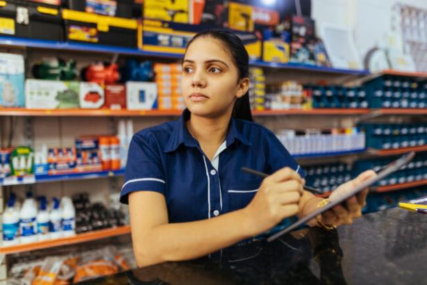 photo of a woman with a clipboard in front of grocery shelves  