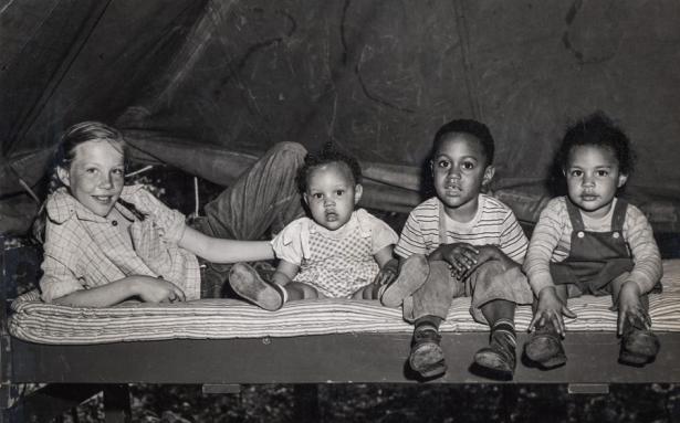 Photo of four children on top of a bed looking at the camera. 