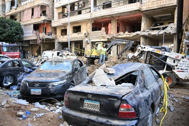 Two cars destroyed by an apparent bomb in from of destroyed buildings.