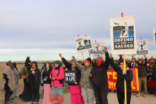 people protesting with raised fists and signs reading "defend the sacred"