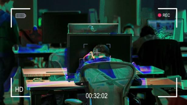 photo of the back of someone at a desk surrounded by surveillance technology.