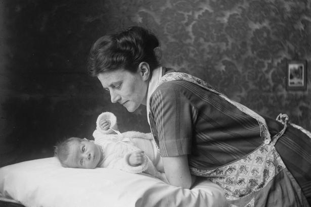 A woman sitting over and holding an infant. 