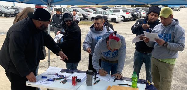 Workers at a table in a parking lot reading and signing