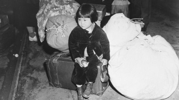 young Japanese-American girl sitting on bag waiting to go to concentration camp