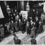 Photo of men in suits and coats standing in front of the union building. 