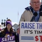 Bernie Sanders at a podium in from of the US Capitol people rallying with signs saying Raise the minimum wage.  Time for $17 and hour.