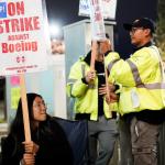 Workers in yellow jackets holding Strike Against Boeing signs.