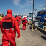 Photo of the backs of suited safety worker walking along a dock.