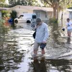 Two people walking through flooded streets with houses in the background.