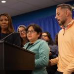 Photo of workers speaking at a press conference with Tish James in the background. 