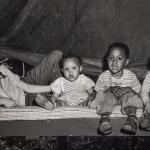 Photo of four children on top of a bed looking at the camera.