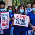 Nurses in masks and blue uniforms with signs - Nurses Against Racism