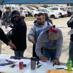 Workers at a table in a parking lot reading and signing