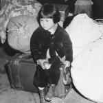 young Japanese-American girl sitting on bag waiting to go to concentration camp