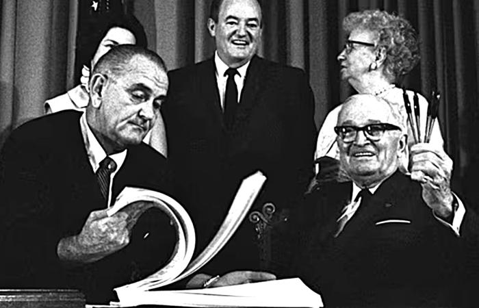 Former President Harry Truman grins at President Lyndon Johnson during the Medicare/Medicaid bill signing ceremony
