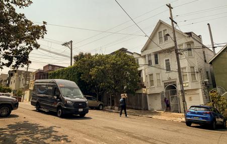 Van parked on a street.  Amazon walking towards a house to deliver a package.n 