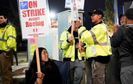 Workers in yellow jackets holding Strike Against Boeing signs.