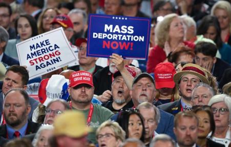 Photo of a Trump rally with people holding "Mass Deportation Now" signs.