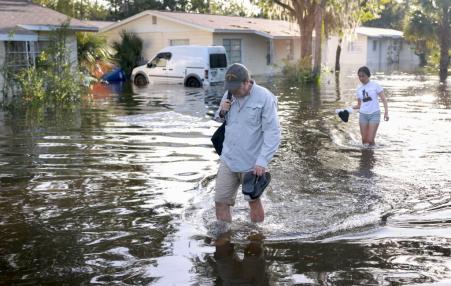 Two people walking through flooded streets with houses in the background.