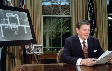 Ronald Reagan sitting in front of an aerial photo of a target in Cuba in March 1983