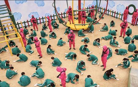 Scene from the Netflix show:  Individuals in green outfits kneeling on the floor.
