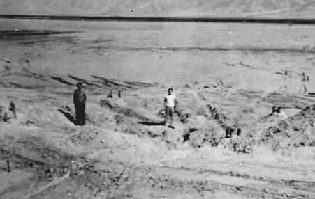 Two men standing at ground zero after the first nuclear bomb test