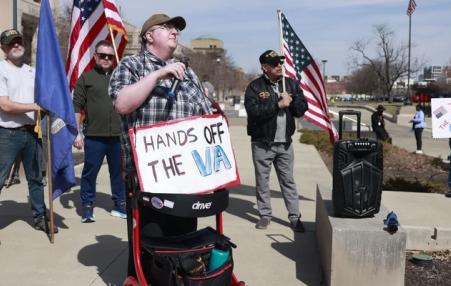 Photo of people marching with signs like, "Hands off the VA". 