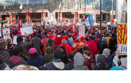 Photo of a massive rally shot from the back with the people facing a building in front and carrying signs. 