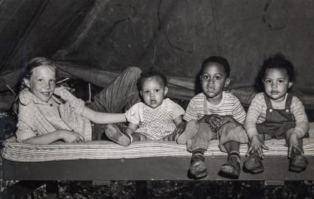 Photo of four children on top of a bed looking at the camera. 