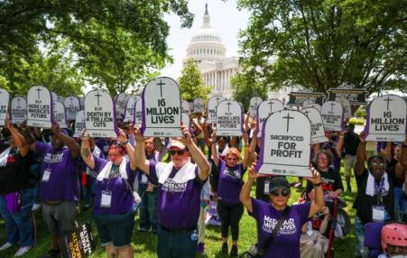 Protestors holding up cardboard signs the shape of a gravestone which reads sacrificed for profits and the like.