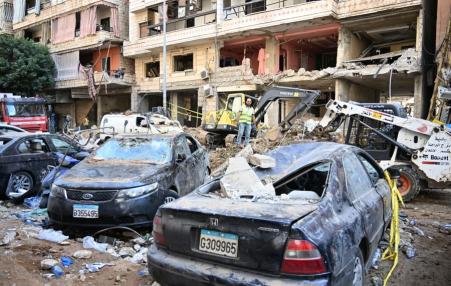 Two cars destroyed by an apparent bomb in from of destroyed buildings.