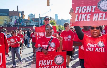 Photo of people marching in red tees and holding signs that say fight like hell 