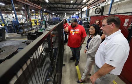 labor secretary and a couple of workers looking over a factory.