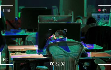 photo of the back of someone at a desk surrounded by surveillance technology.