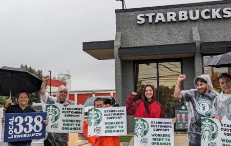 A few Starbucks customers and union allies stand in front of a Starbucks store with signs saying they support Starbucks workers. ta m  