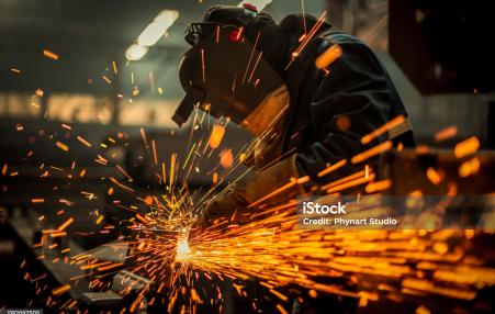 Sparks shooting up from a work table towards a worker with face protection.