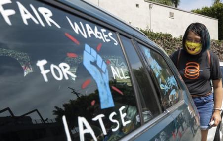A woman standing behind a van with the following painted on the window:  Fair wages for IATSE