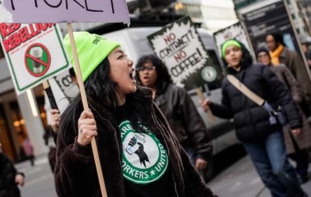 Workers with signs in the foreground with a Starbucks in the background.