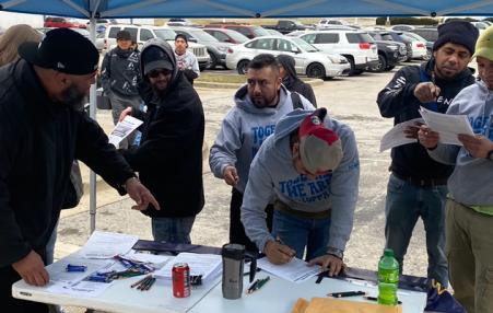 Workers at a table in a parking lot reading and signing